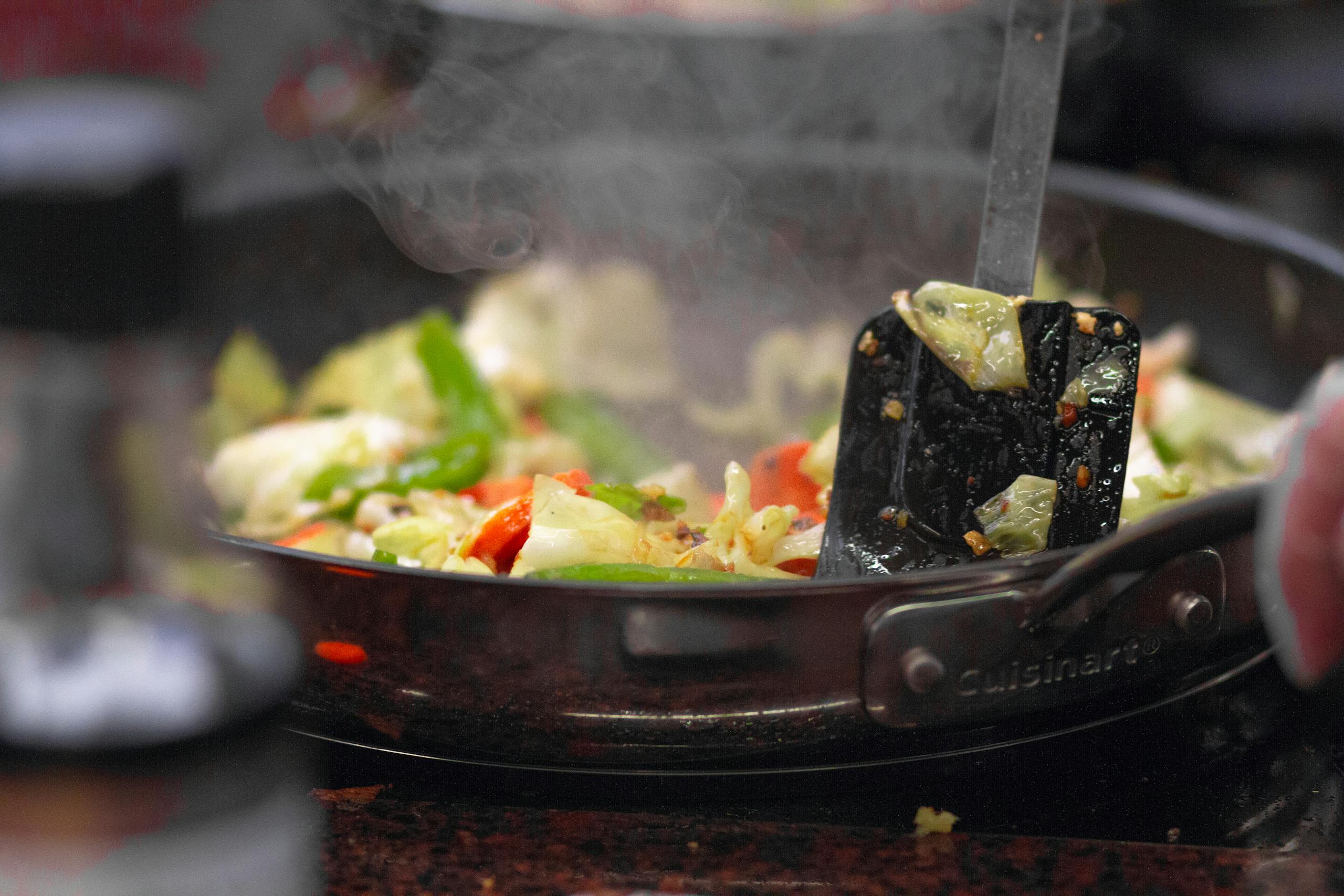 A vibrant stir fry of fresh vegetables sizzling in a pan, releasing steam.