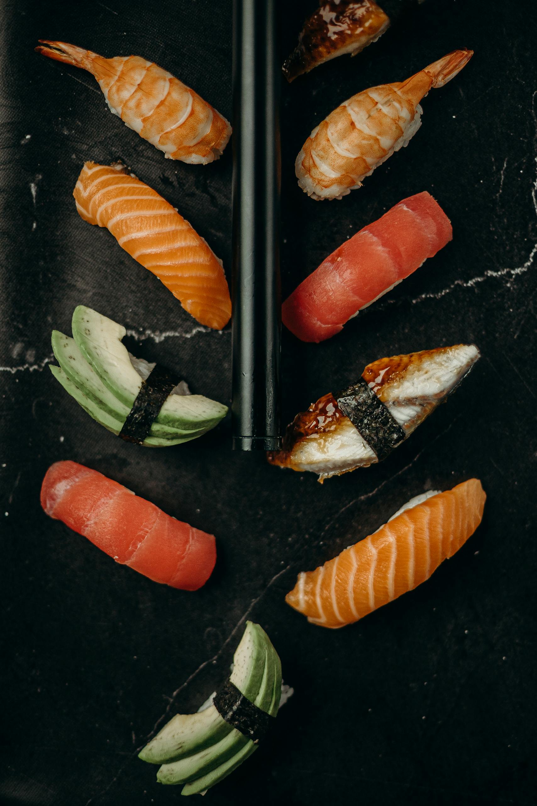 Elegant flat lay of assorted sushi pieces on a dark marble surface with chopsticks.